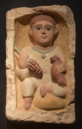 Egyptian boy with a branch of grapes and a small dog, Coptic limestone tomb stele from Antinoupolis,